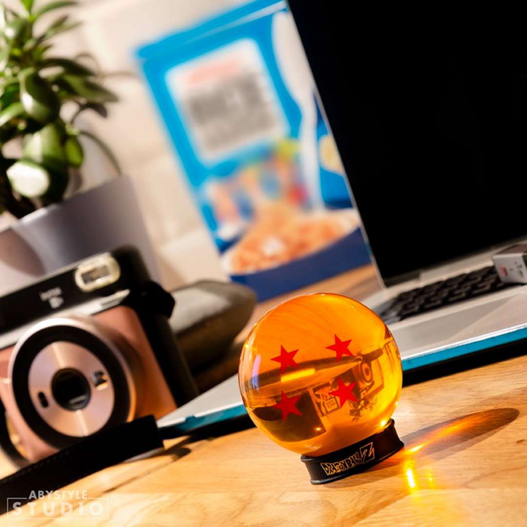 ABYstyle Dragon Ball Z 4 stars Dragon Ball acrylic replica on display base, shown on a wooden desk with a laptop, camera, and plant in a lifestyle workspace setting.