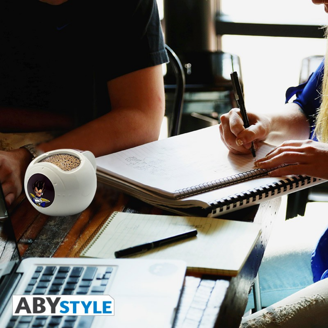 ABYstyle Dragon Ball Z 3D ceramic mug shaped like Vegeta’s Saiyan space pod with heat-sensitive Vegeta design, shown on a work desk with people using computers, perfect for anime fans at the office or home workspace.