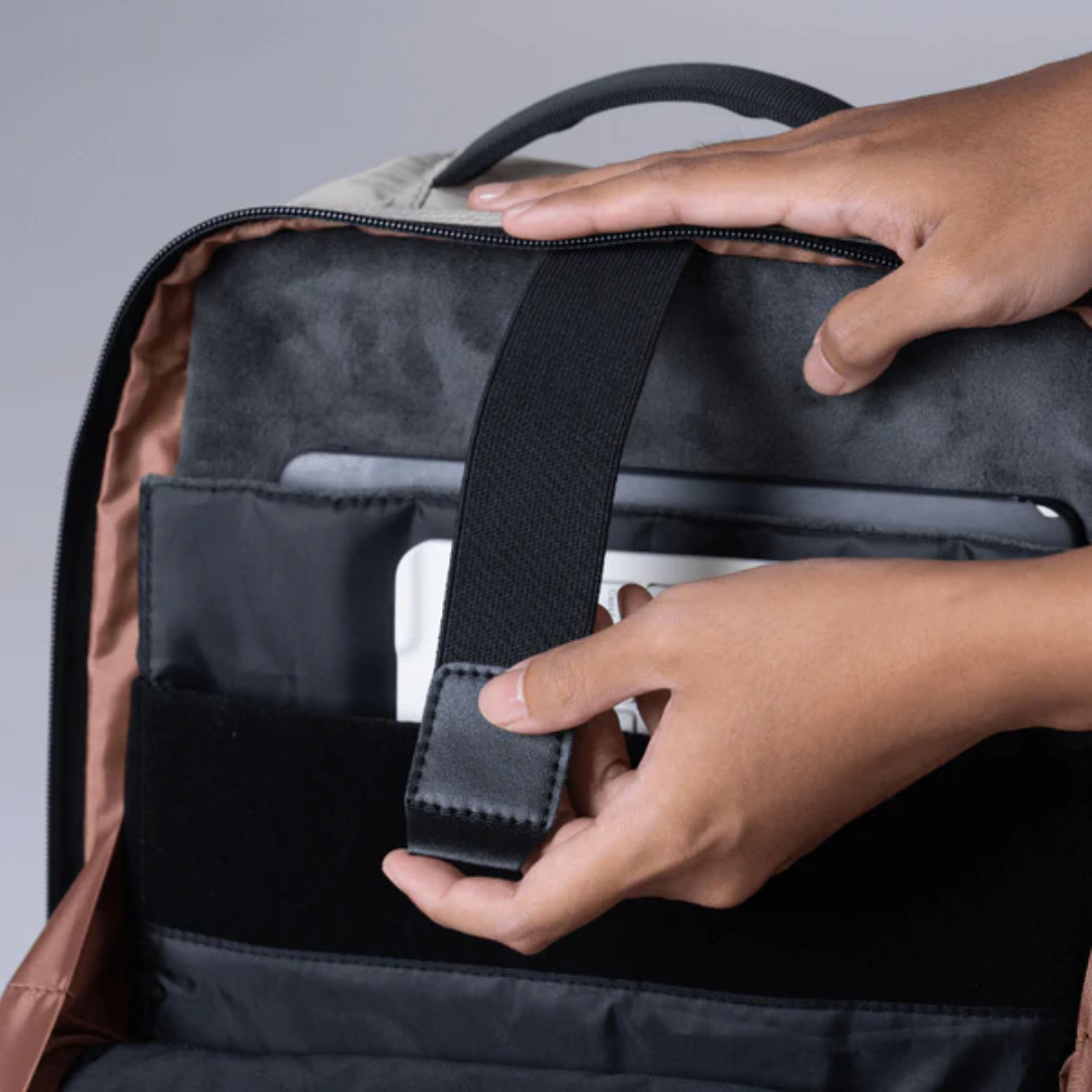 Close-up of hands securing a laptop and tablet in a backpack using a padded strap