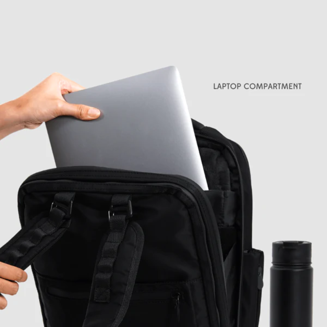 Hand placing a silver laptop into the padded laptop compartment of a black backpack.