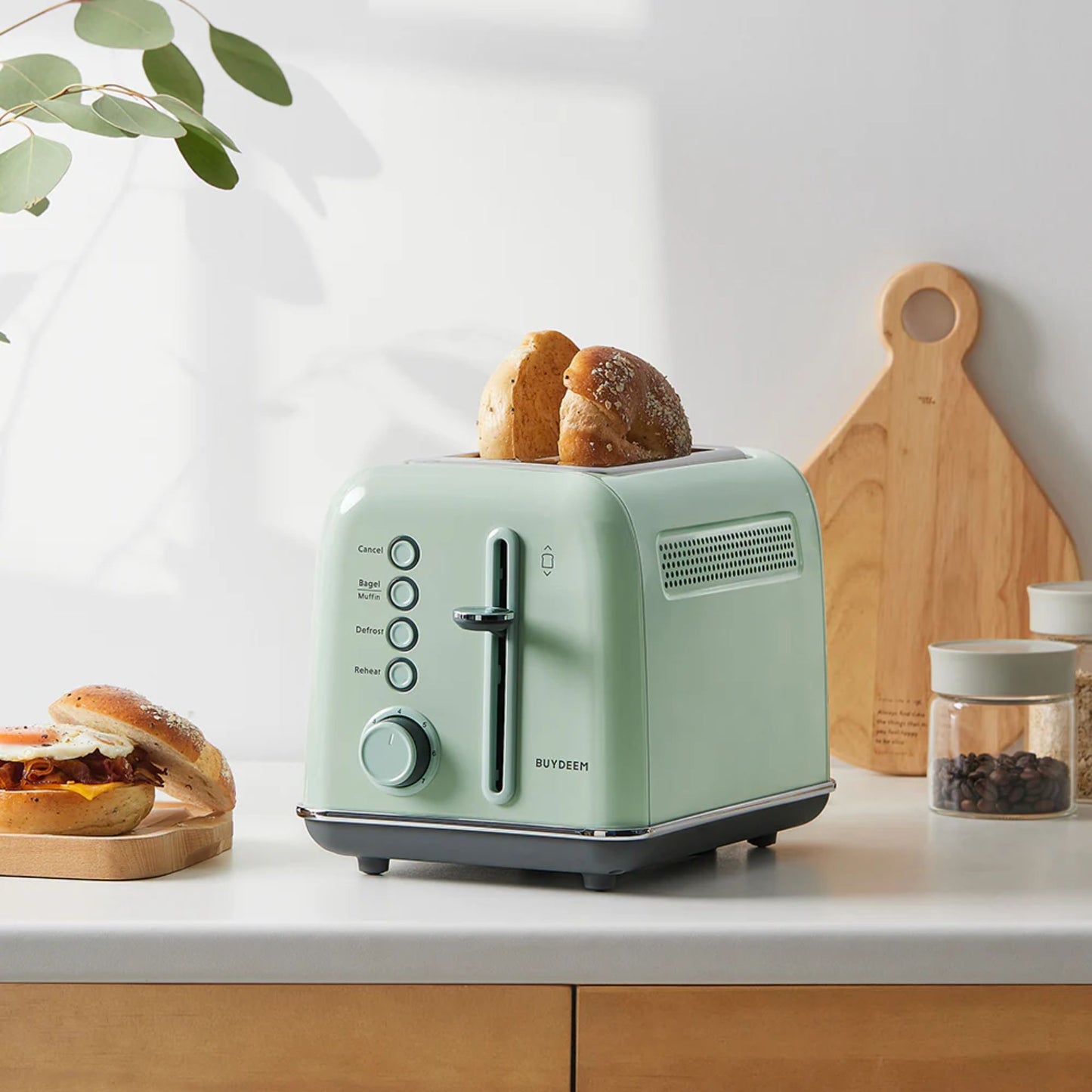 Buydeem 2-Slice Toaster Cozy Greenish toasting bagels on kitchen counter with breakfast sandwich and cutting board