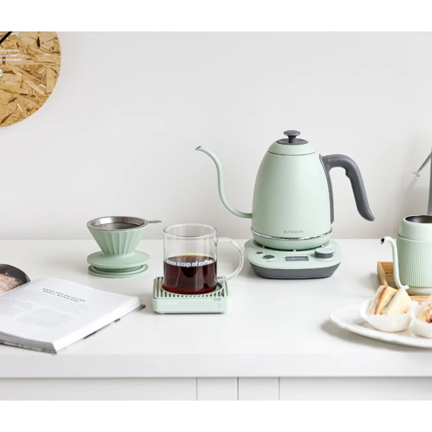 Buydeem mint green electric kettle with matching pour over coffee maker, glass mug, and pastries on a white kitchen countertop in a stylish modern breakfast scene
