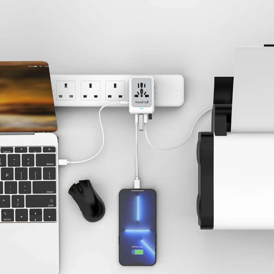 Travelmall universal multi-port USB power adapter plugged into a power strip, charging a smartphone, laptop, and printer at a modern workstation, illustrating simultaneous device charging for travel or office use.