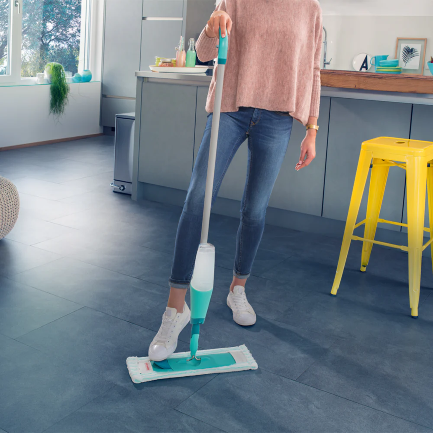 Person mopping a modern kitchen floor with a Leifheit Comfort Easy Spray XL refillable microfiber spray mop.