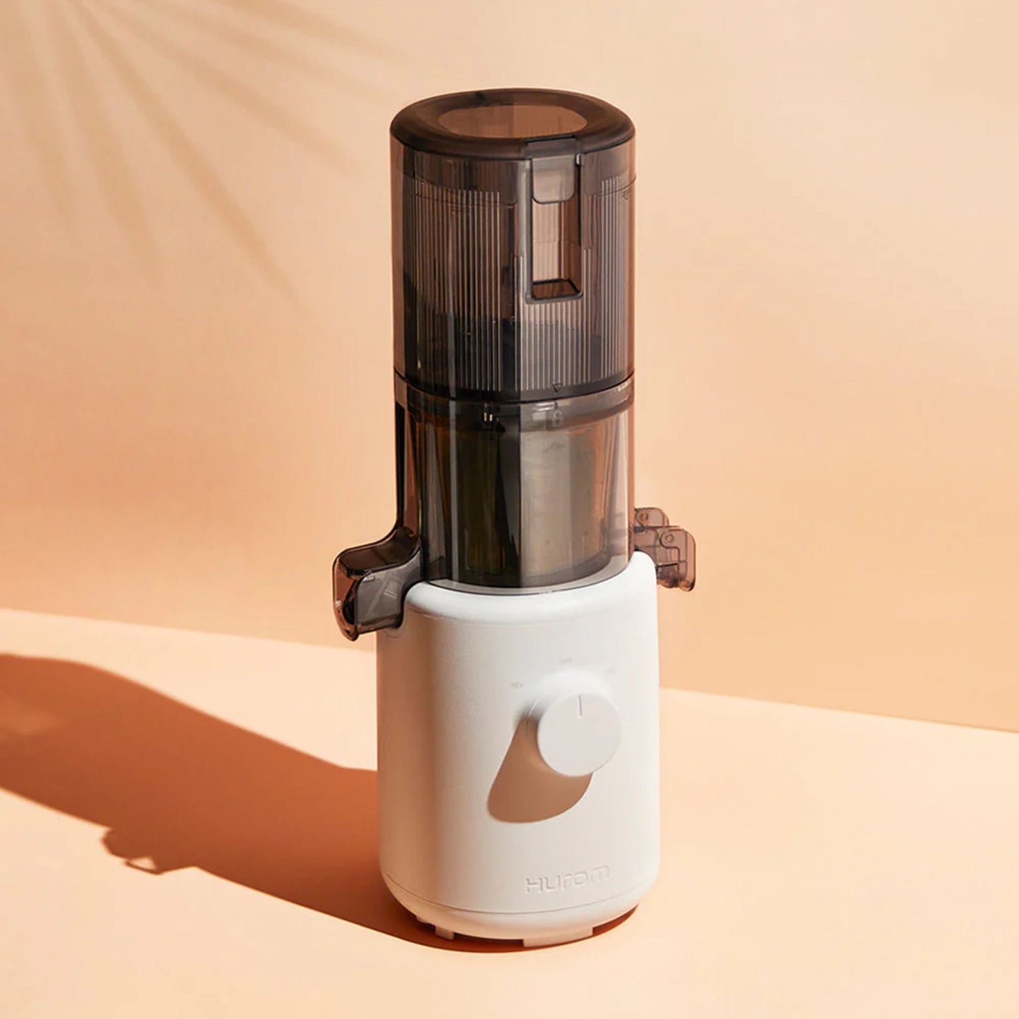 Hurom H310A Slow Juicer white compact model, modern BPA-free juicer, lifestyle front view with sunlit background and creative shadow