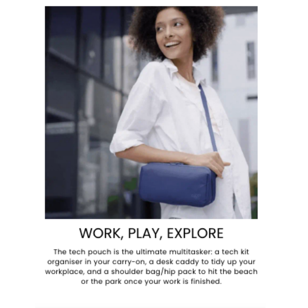 Person wearing a white shirt and carrying a rectangular navy blue tech pouch with a shoulder strap, standing outdoors in an urban setting.