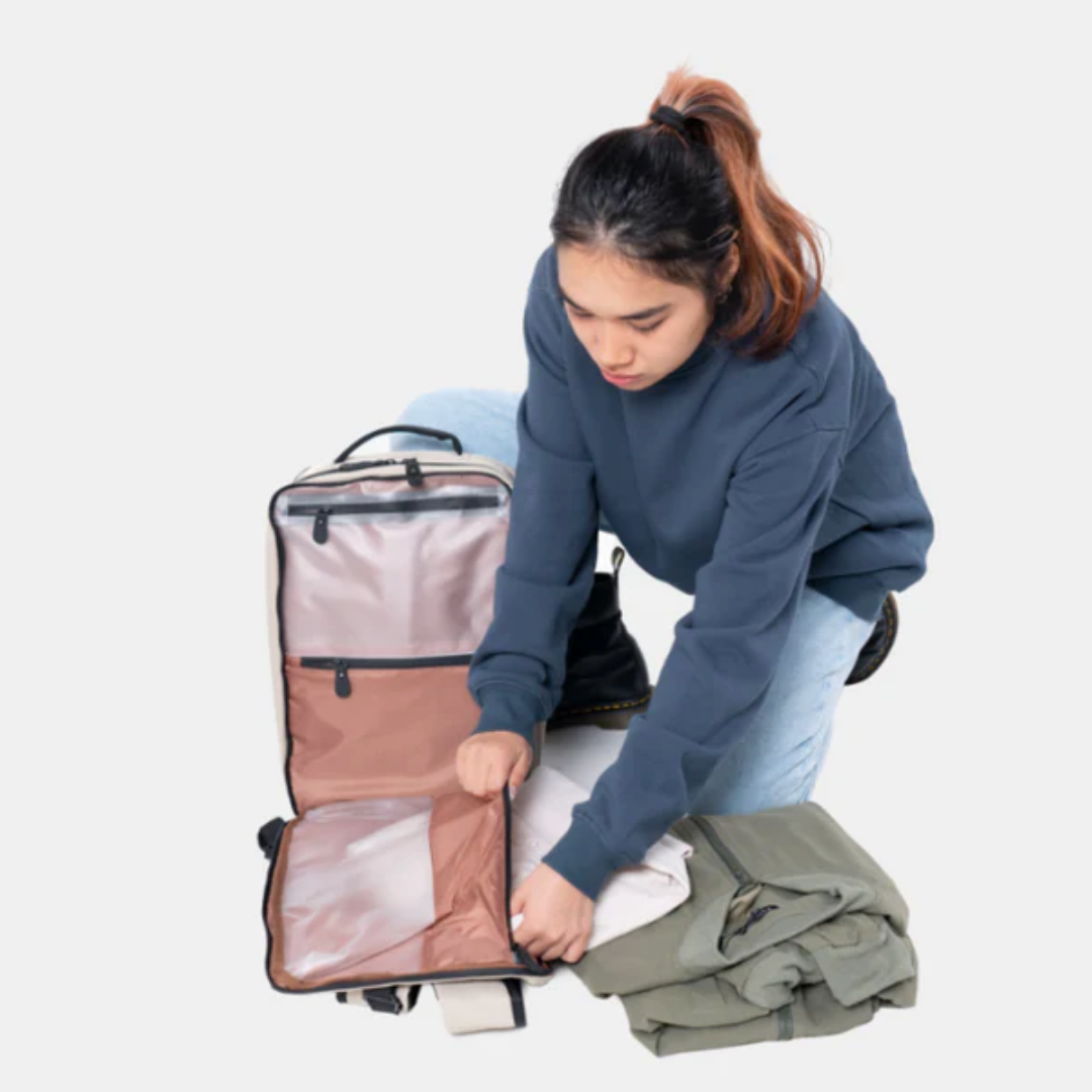 Person packing clothes into an open backpack with organized compartments, preparing for travel.