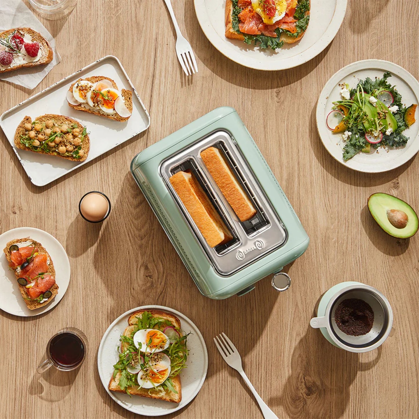 Top view of Buydeem 2-Slice Toaster Cozy Greenish surrounded by healthy breakfast toast, avocado, eggs, and salad on wooden table
