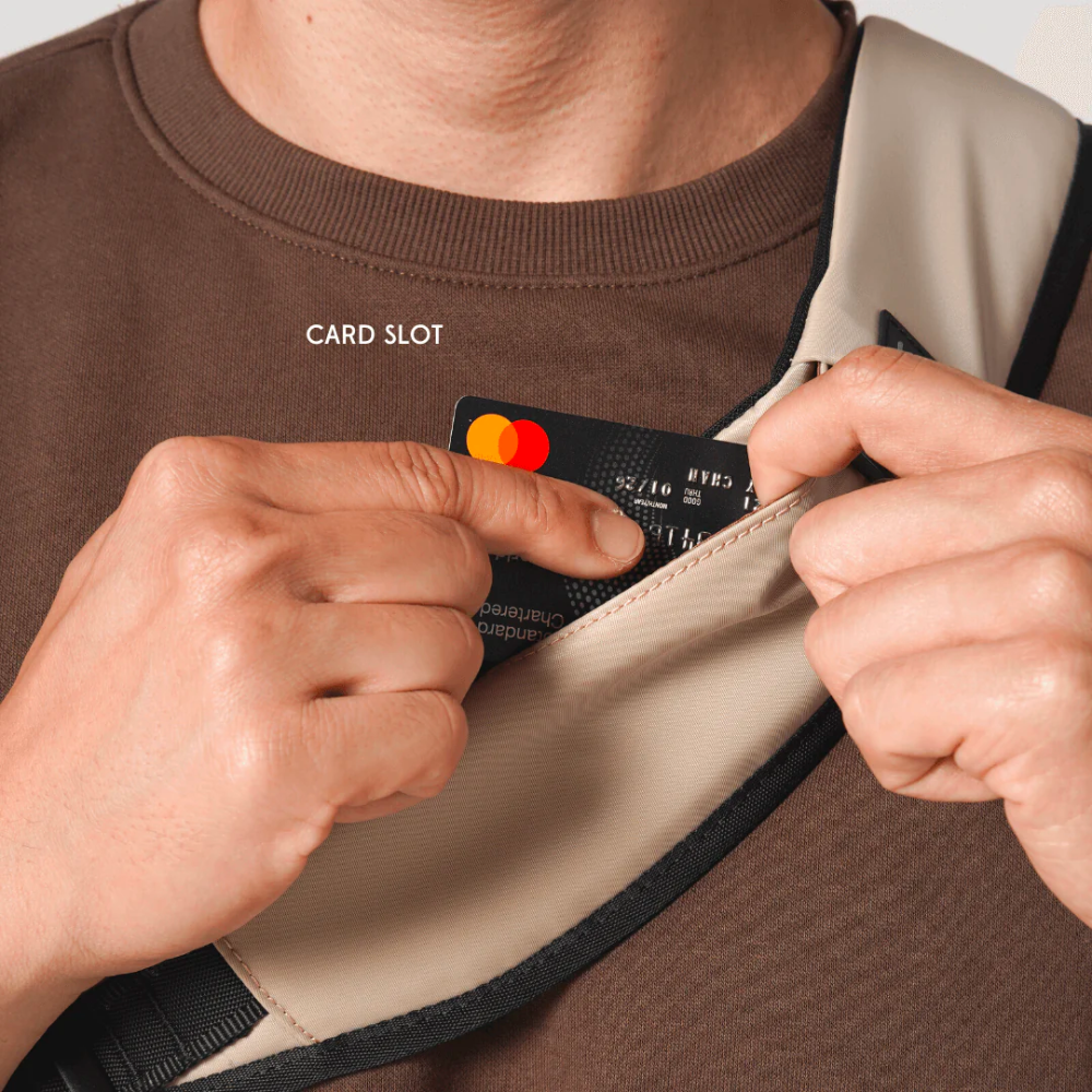 Man inserting Mastercard into card slot pocket on Bold beige crossbody sling bag strap, secure and convenient access for travel and daily use