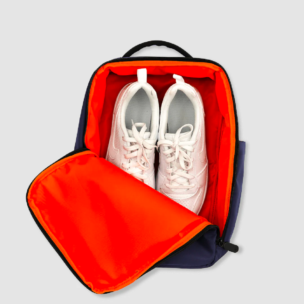 Bold Quiver 13L navy blue sports backpack with bright orange interior shoe compartment, open to display white sneakers, top handle visible, ideal for gym and travel organization