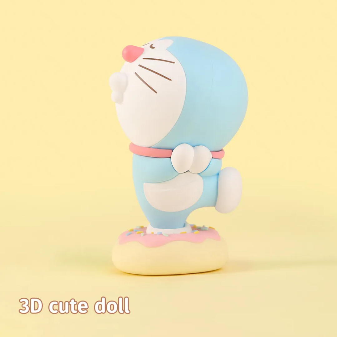 3D Doraemon cute doll figure with pink nose and collar, standing on a donut-shaped base with pink icing and colorful sprinkles, on a pastel yellow background with "3D cute doll" text