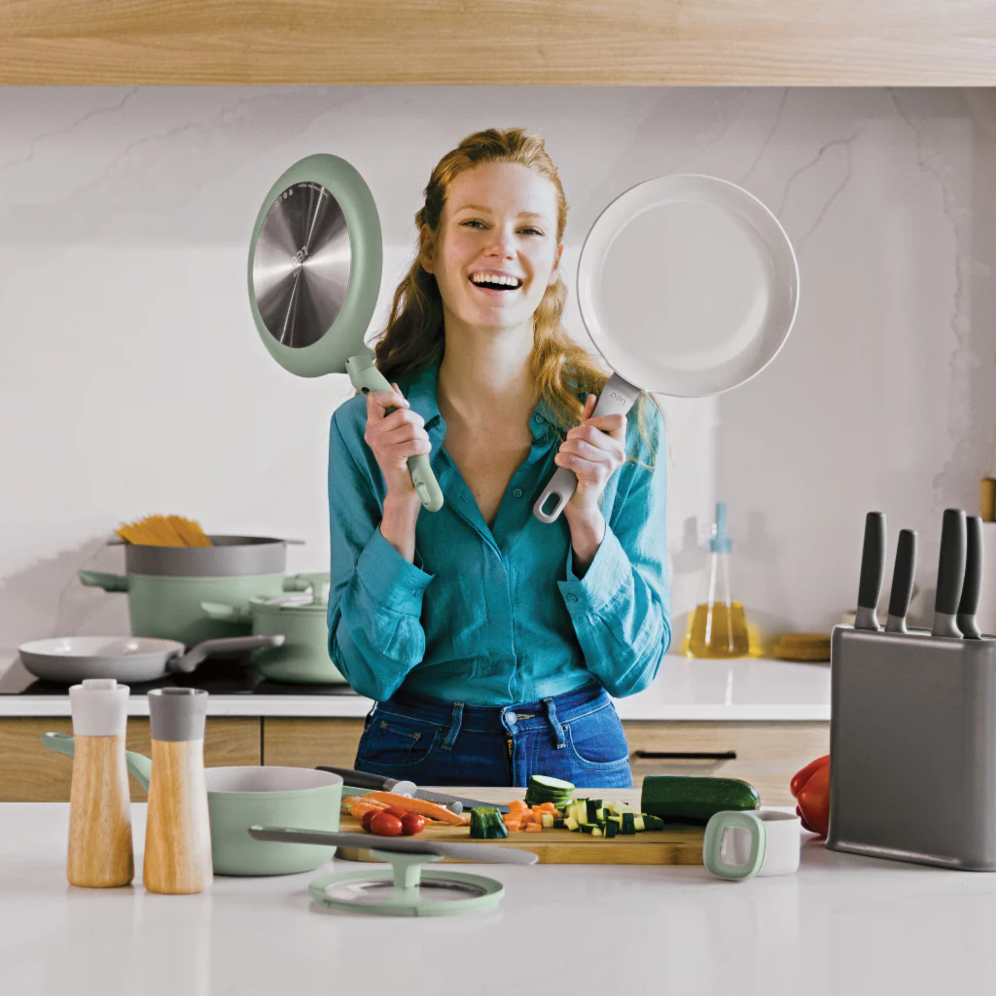 Smiling woman in a modern kitchen showcasing BERGHOFF Balance eco-friendly cookware, including non-stick pans and saucepan, ideal for healthy home cooking