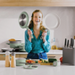 Smiling woman in a modern kitchen showcasing BERGHOFF Balance eco-friendly cookware, including non-stick pans and saucepan, ideal for healthy home cooking