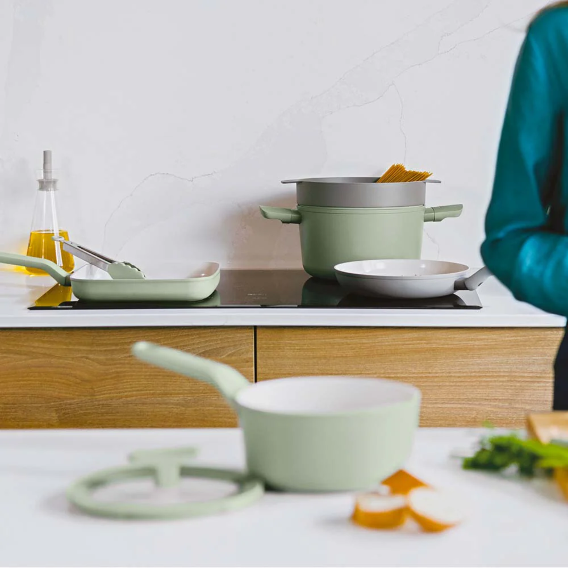 BergHOFF Balance sage green non-stick cookware on induction hob, including saucepan, grill pan and pasta pot in modern kitchen setting.