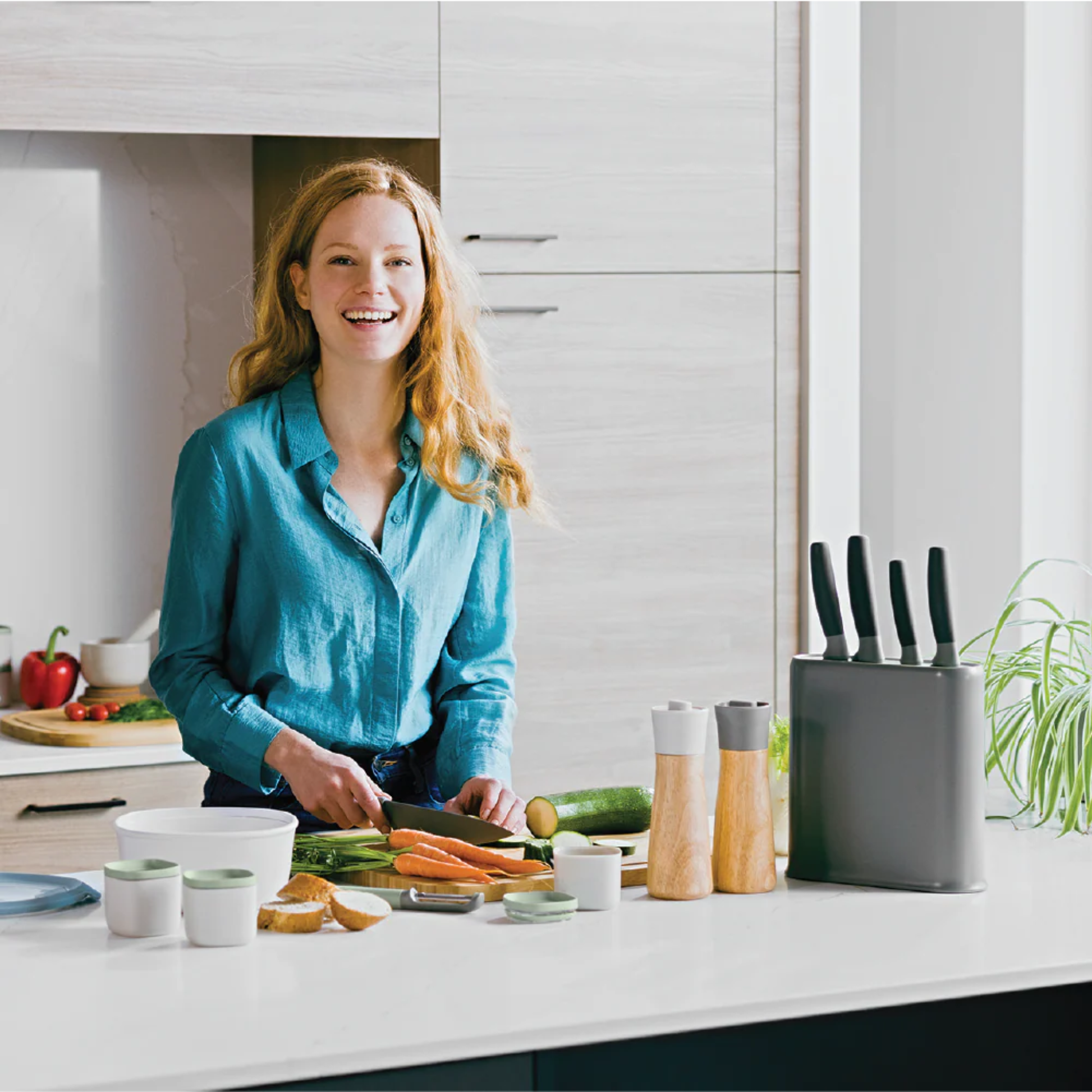 Smiling woman chopping vegetables in a bright modern kitchen with a grey BergHOFF knife block set on the countertop.