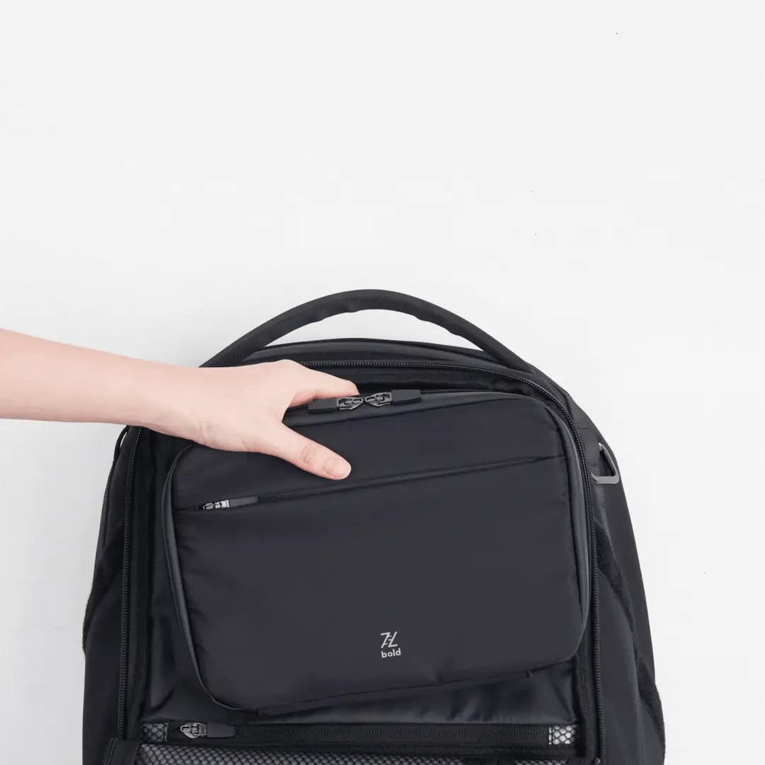 Hand removing a detachable black organizer pouch from the front compartment of a Bold black backpack, highlighting modular storage and easy organization for travel or daily use.