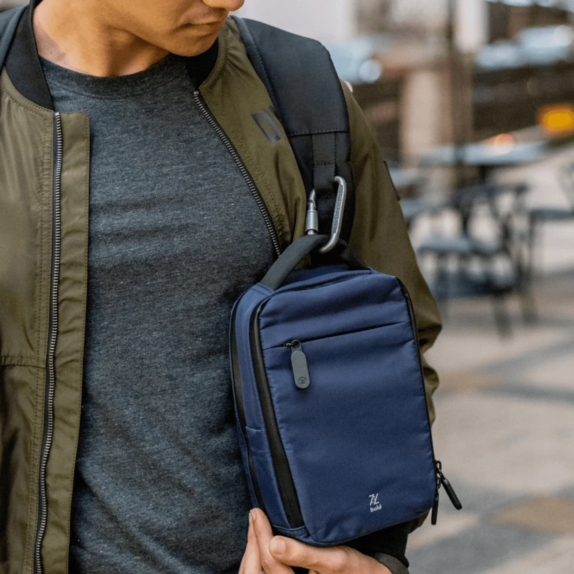Bold Mimic Sling Bag in navy blue, clipped to shoulder strap in an outdoor city setting; stylish, practical choice for travel and daily essentials.