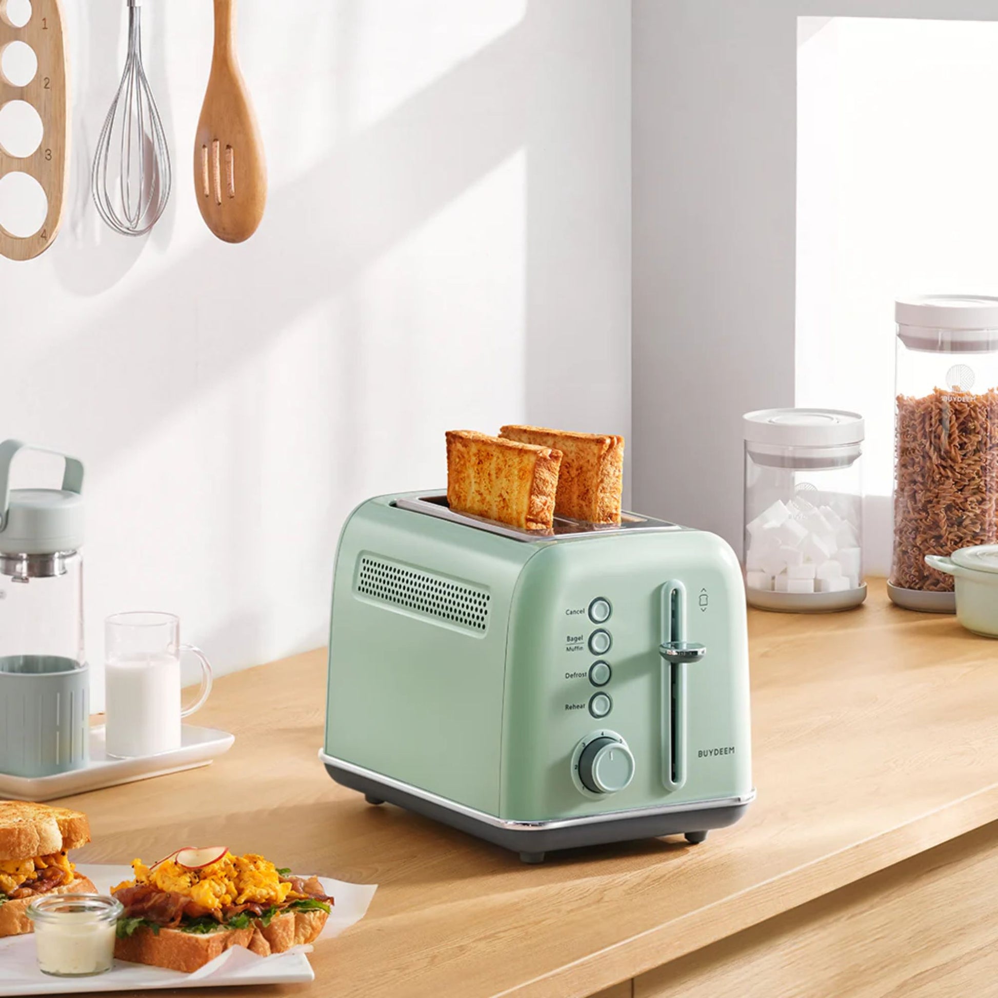 Buydeem 2-Slice Toaster Cozy Greenish with golden toast on kitchen counter, next to breakfast sandwiches, milk, and cereal jars