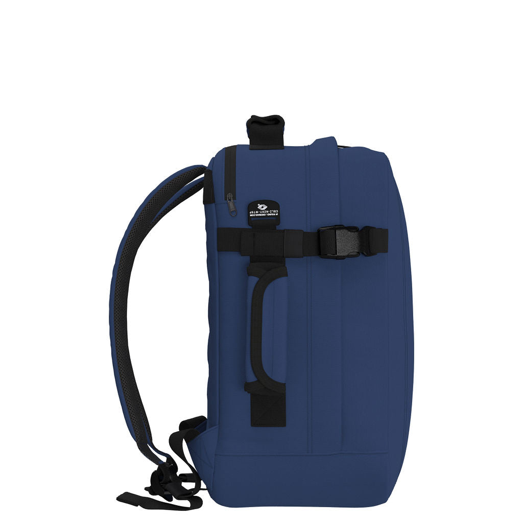 Side view of CabinZero Classic Tech Bag 28L in Navy Blue highlighting padded side handle, compression strap, and Tracer tag—designed for secure, comfortable, and versatile carry during travel or daily commutes.