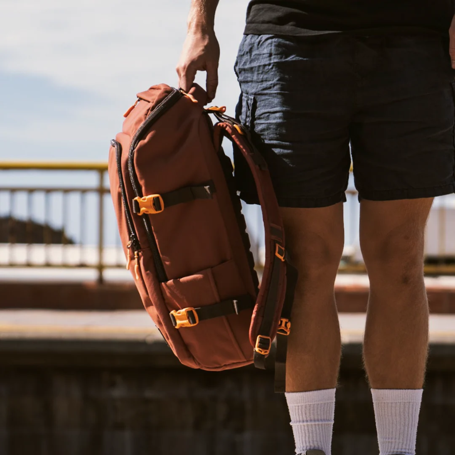 CabinZero ADV Pro 32L backpack in Saigon Coffee brown being hand-carried outdoors, durable travel bag with side compression and padded straps for adventure