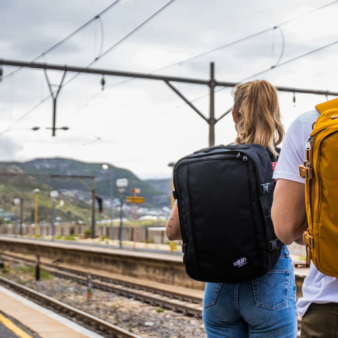 CabinZero Classic black travel backpack worn by female traveler at outdoor train station, ideal for adventure and minimalist travel.