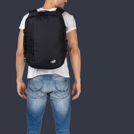 CabinZero Classic black travel backpack worn by male model with white t-shirt and jeans on dark background, ideal for minimalist travel.