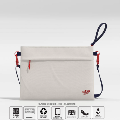Front view of a CabinZero Classic Sacoche 2.5L pouch in Cloud Nine color with red zipper and navy blue strap, displayed on a light background. Six feature icons below indicate RFID blocking, lifetime warranty, recycled material, Kindle Paperwhite compatibility, ultra light weight, and water resistance
