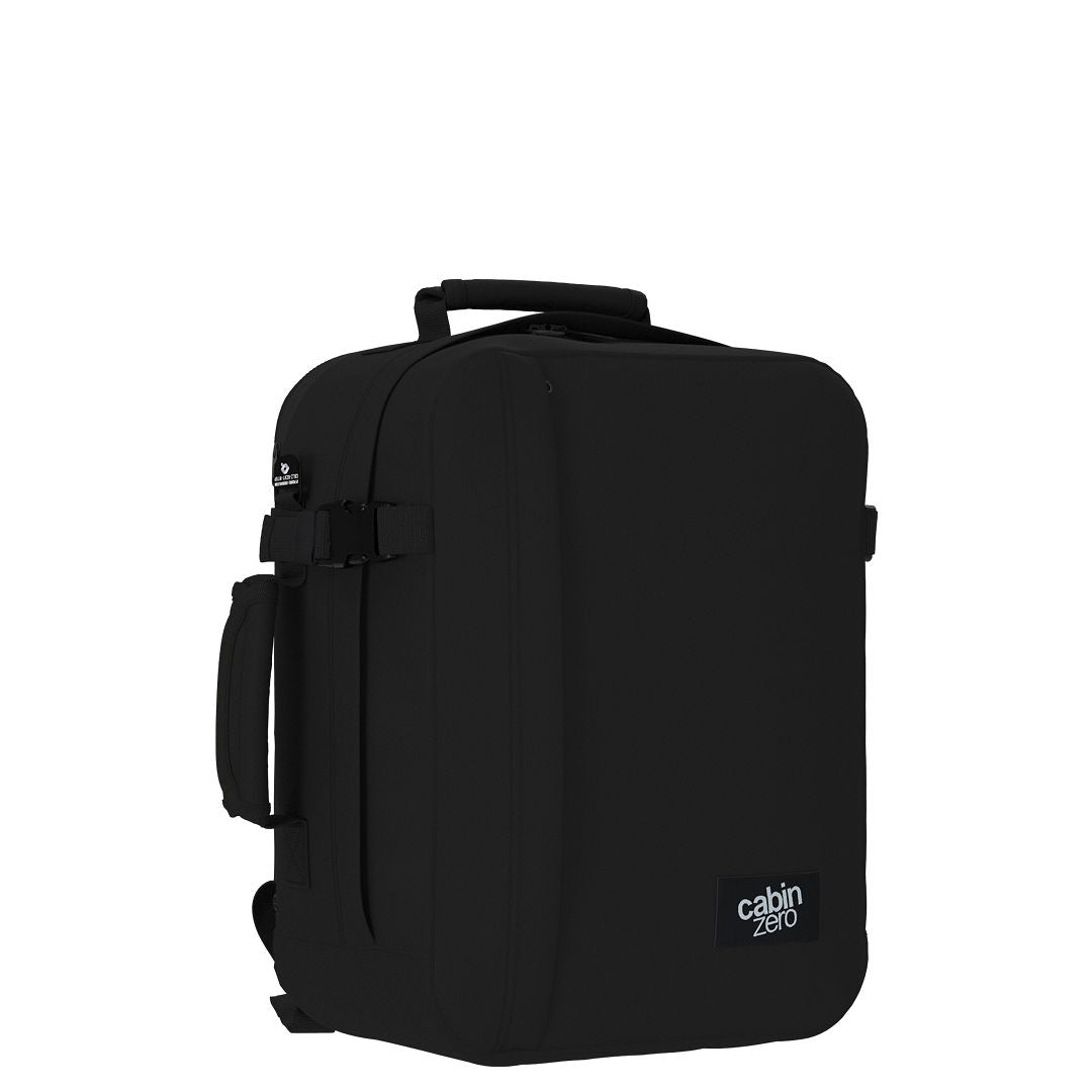 Angled view of CabinZero Classic Tech Bag 28L in Absolute Black showing side handle, compression straps, and sleek profile—ideal carry-on backpack for tech gear and travel needs