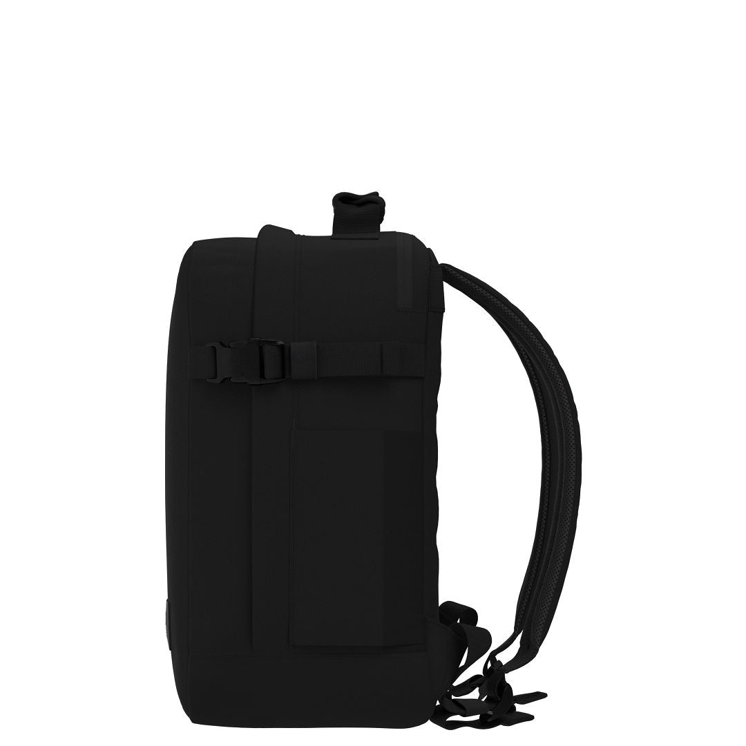 Profile view of CabinZero Classic Tech Bag 28L in Absolute Black displaying slim shape, adjustable compression strap, and side pocket—perfect for tech gear and minimalist travel.