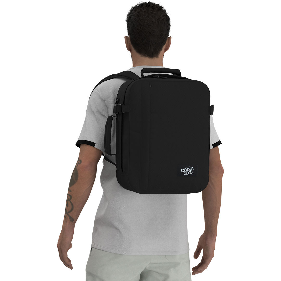 Man wearing CabinZero Classic Tech Bag 28L in Absolute Black—carry-on travel backpack with dedicated laptop sleeve, water bottle pocket, and ergonomic design, ideal for tech-savvy travelers and commuters.