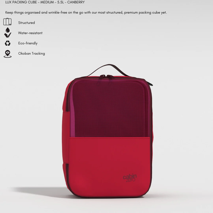 A medium-sized, structured packing cube in deep red and berry tones, labeled "cabin zero" at the lower right. The cube features a mesh front panel, a top handle, and a zipper closure. Above the cube, icons and text highlight its structured design, water resistance, eco-friendly materials, and Okoban tracking.