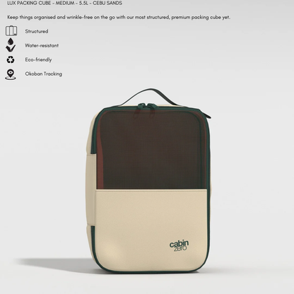 A medium-sized, structured packing cube in beige and dark green, labeled "cabin zero" at the bottom right. The cube features a mesh front panel, a handle on top, and a zipper closure. Icons and text above highlight its features: structured design, water-resistant, eco-friendly materials, and Okoban tracking