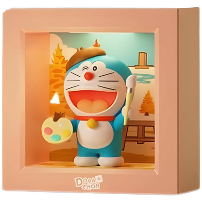 Doraemon collectible figure dressed as an artist, winking and smiling, holding a paintbrush and a colorful palette, wearing a brown beret, displayed inside a peach-colored frame with an autumn landscape painting in the background