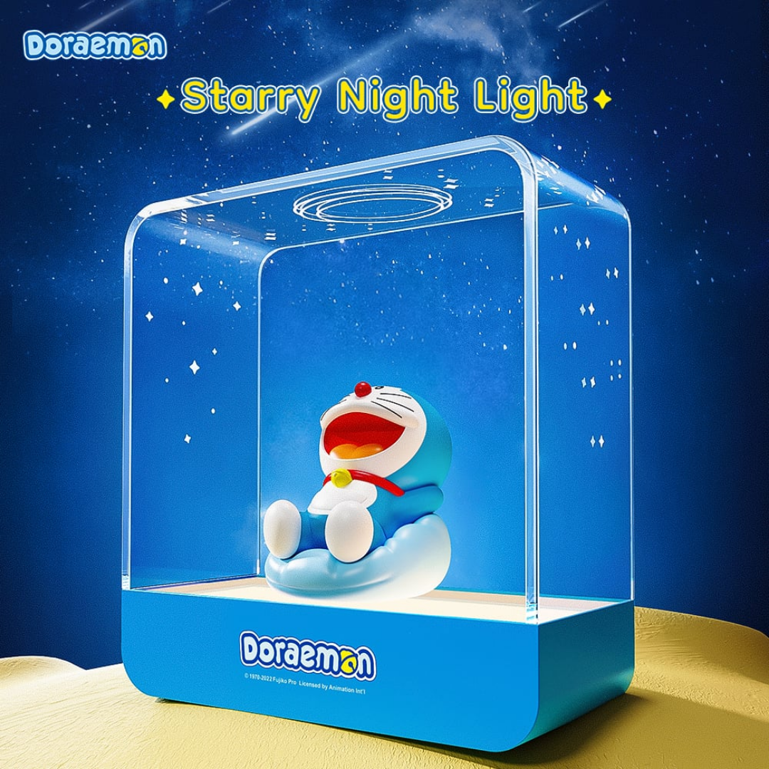 Doraemon Starry Night Light featuring a smiling Doraemon figure sitting on a blue cushion inside a transparent rectangular lamp, projecting star patterns with a dreamy night sky background and "Starry Night Light" text above