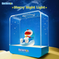 Doraemon Starry Night Light featuring a smiling Doraemon figure sitting on a blue cushion inside a transparent rectangular lamp, projecting star patterns with a dreamy night sky background and "Starry Night Light" text above