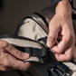 Close-up of a person fastening a black strap buckle on a beige backpack.