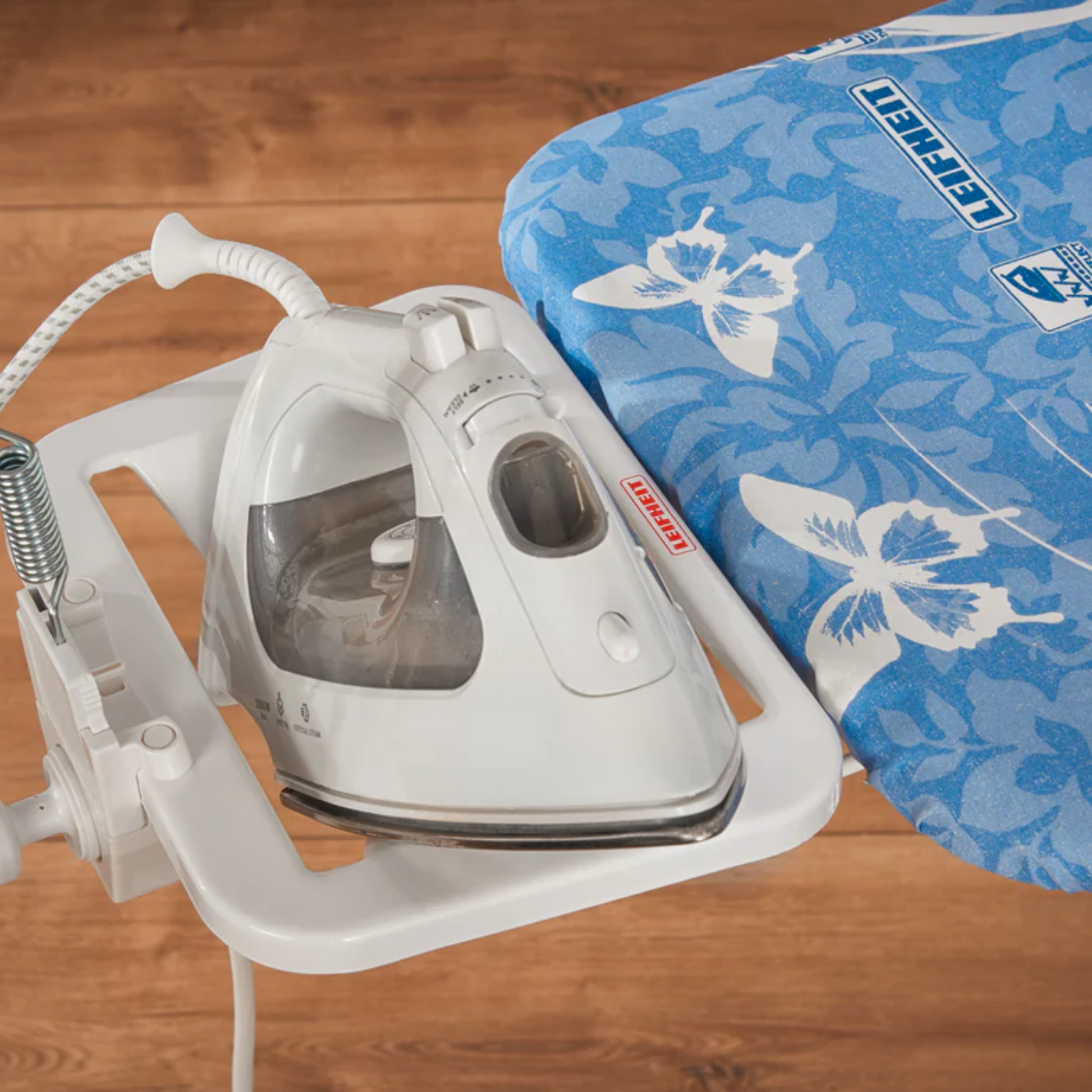 Leifheit AirBoard Compact ironing board with blue butterfly cover and parked steam iron on integrated iron rest.