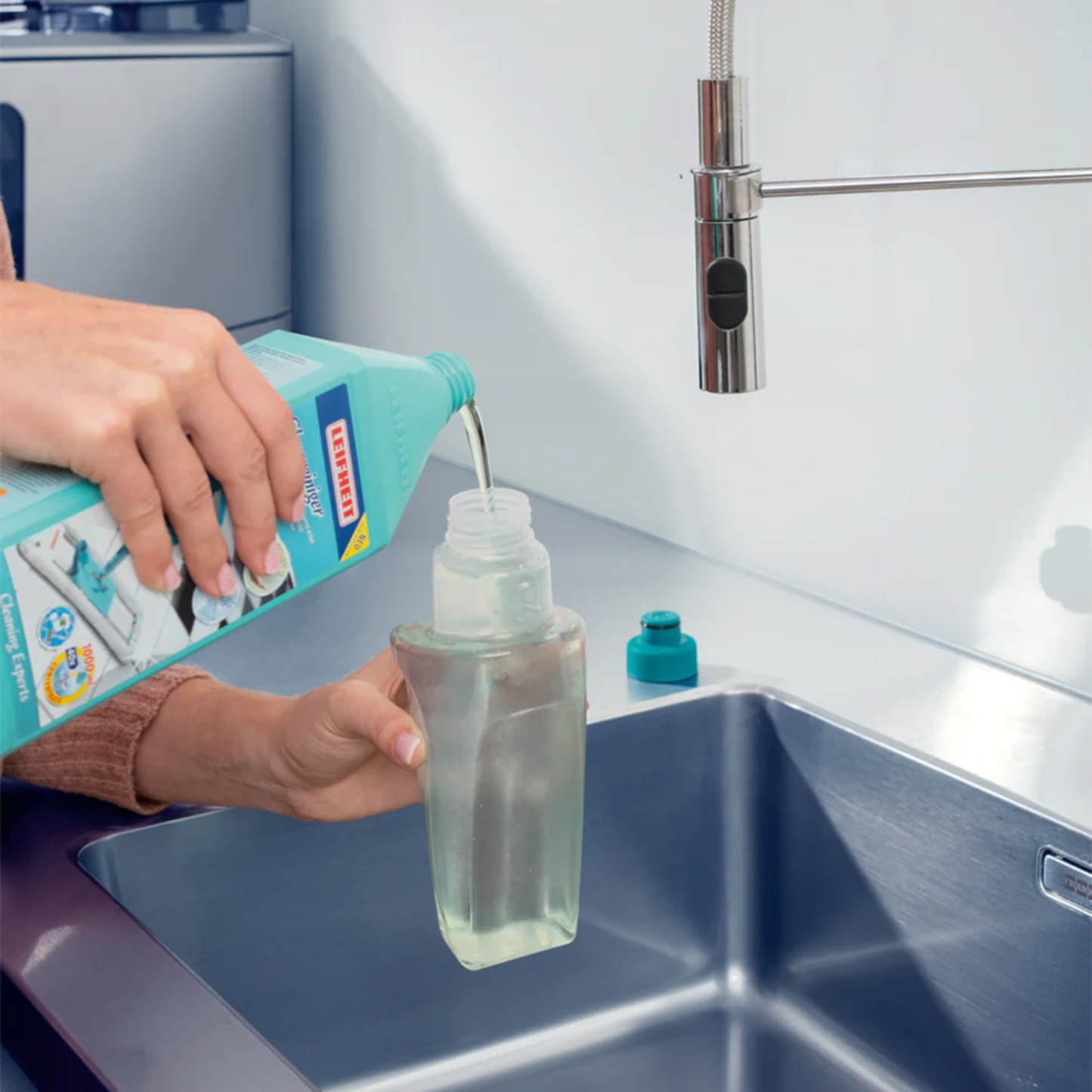 Person pouring Leifheit floor cleaner into a refillable spray mop cartridge over a stainless steel kitchen sink.