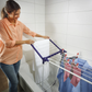 Woman using Leifheit Pegasus 120 Solid Compact clothes drying rack placed across a bathtub to dry shirts and socks indoors