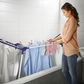 Woman hanging towel on Leifheit Pegasus 120 Solid Compact clothes drying rack set across a bathtub for indoor laundry drying