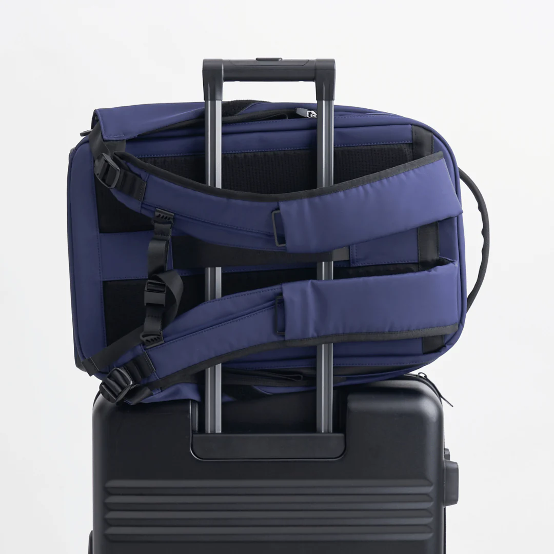 Navy backpack securely attached to a black suitcase handle, showing padded shoulder straps and travel-friendly design for easy airport transit.