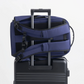 Navy backpack securely attached to a black suitcase handle, showing padded shoulder straps and travel-friendly design for easy airport transit.