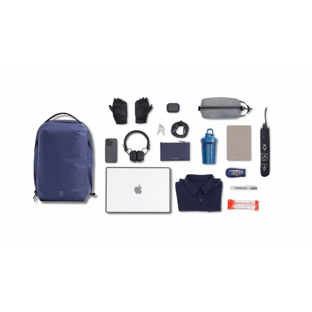 Flat lay of navy blue backpack and everyday essentials including laptop, headphones, gloves, water bottle, shirt, tech accessories, and snacks on a white background.