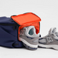 Navy backpack with bright orange shoe compartment, shown storing a pair of gray sneakers, ideal for gym, travel, or keeping shoes separate from other essentials.