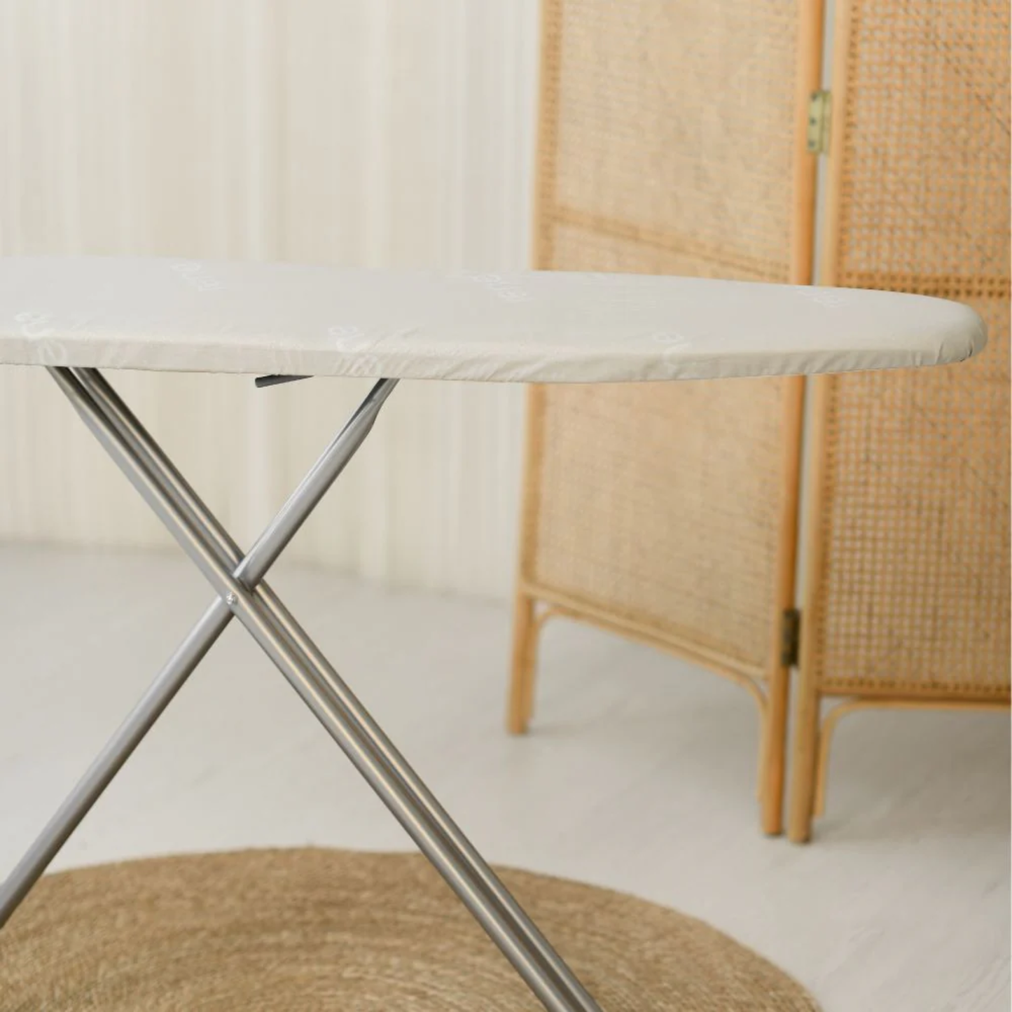 Close-up of RENE classic ironing board with padded white top and sturdy silver X-shaped legs on a light floor.