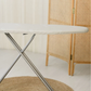 Close-up of RENE classic ironing board with padded white top and sturdy silver X-shaped legs on a light floor.