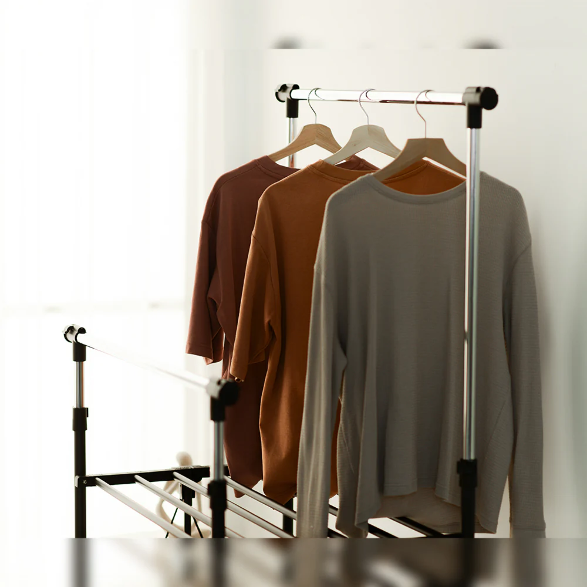 Close-up of RENE Ocho expandable laundry drying rack with three long-sleeve tops hanging on the upper bar, showing indoor clothes drying in a bright bedroom.