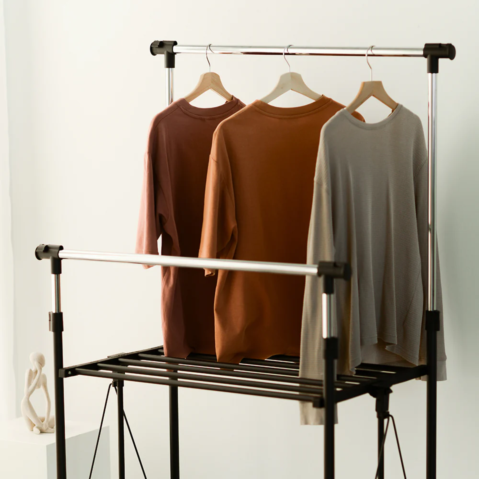 Front view of RENE Ocho expandable laundry drying rack with three long-sleeve tops hanging on wooden hangers, showing upper bar and middle rails for indoor clothes drying.