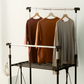 Front view of RENE Ocho expandable laundry drying rack with three long-sleeve tops hanging on wooden hangers, showing upper bar and middle rails for indoor clothes drying.