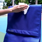 Hand wiping the front flap of a blue Rolser Plegamatic shopping trolley outdoors, showing easy-to-clean water-resistant fabric with logo.